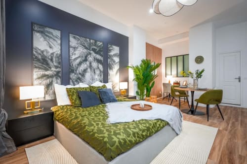 Modern apartment bedroom in Bordeaux with olive green bedding, dark accent wall, palm artwork, and work desk area