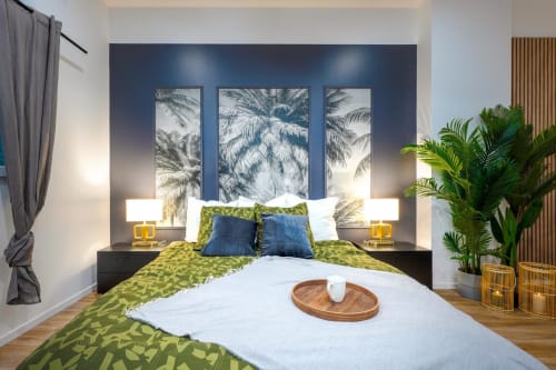 Modern bedroom at Wellkhome Bordeaux with blue accent wall, palm art, green bedding, and tropical plants
