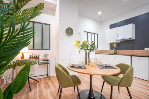 Modern Urban Chic apartment dining area at Wellkhome Bordeaux with kitchen, green chairs, wooden table, and plants