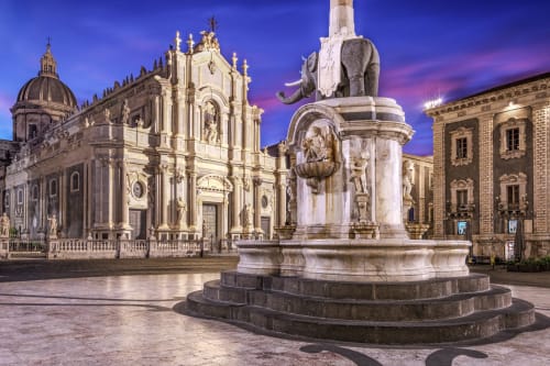 La storica Piazza Duomo di Catania al crepuscolo, con la sontuosa chiesa barocca e il monumento della fontana dell'elefante