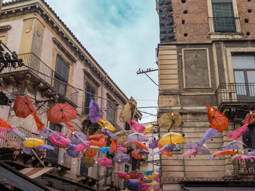Ombrelli colorati sospesi tra gli edifici storici di Catania, Sicilia, vicino all'Apartment 4 Elementi