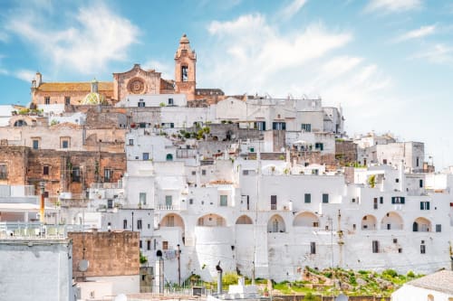 Whitewashed hilltop town of Fasano with church tower, terracotta roofs, and Mediterranean architecture under blue sky