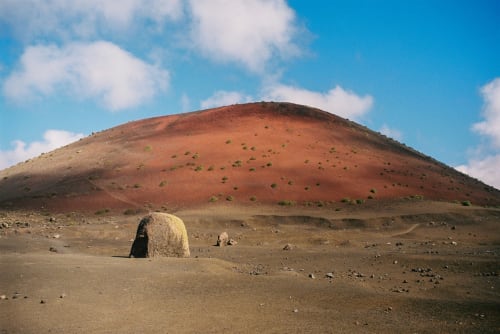 Paisaje volcánico cerca de Finca de La Gería en Yaiza con cono de ceniza roja y vegetación dispersa