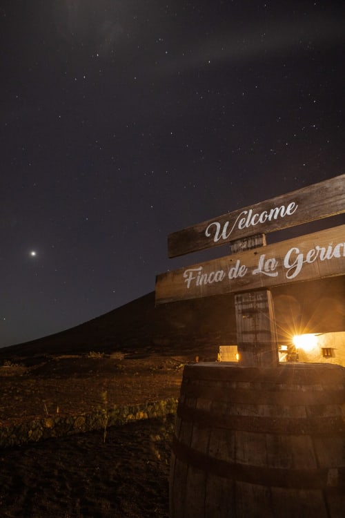 Cartel de bienvenida de madera de Finca de La Geria al anochecer bajo cielo estrellado, Yaiza