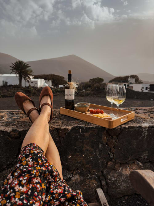 Woman relaxing with wine and charcuterie overlooking volcanic mountains at Finca de La Geria, Lanzarote