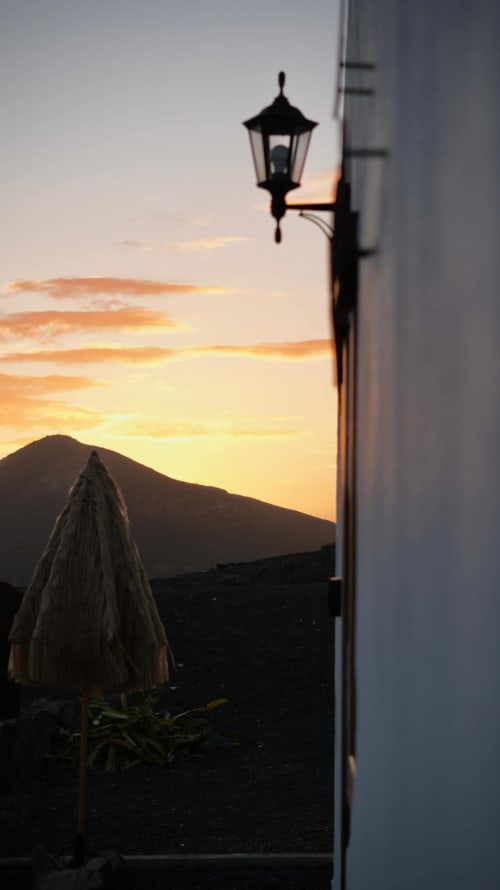 Vista del atardecer desde Finca de La Geria en Yaiza con linterna silueteada y paisaje montañoso al anochecer