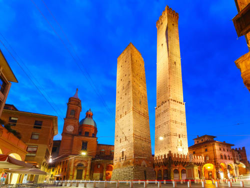 Due torri medievali illuminano la storica Piazza Maggiore di Bologna al tramonto, monumenti iconici vicino ad Ap Appartamenti Bologna
