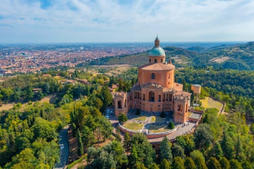 Vista aerea della Basilica di San Luca che domina Bologna, con la chiesa dal tetto rosso, colline verdi e lo skyline della città