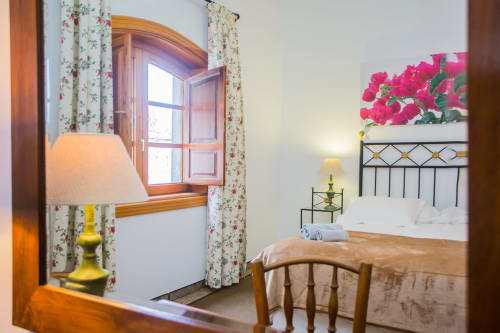 Bright bedroom at Finca de La Geria cottage in Yaiza with floral curtains, wooden furniture, pink flowers, and garden view
