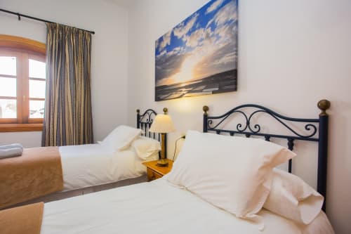 Spacious bedroom at Finca de La Geria cottage in Yaiza with wrought iron bed, white linens, landscape artwork, and garden