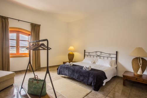 Bright bedroom at Finca de La Geria cottage with wrought-iron bed, orange-framed window, and garden views