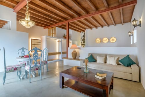 Spacious El Granero cottage living area at Finca de La Geria with wooden beams, cream sofa, dark wood table, and garden views