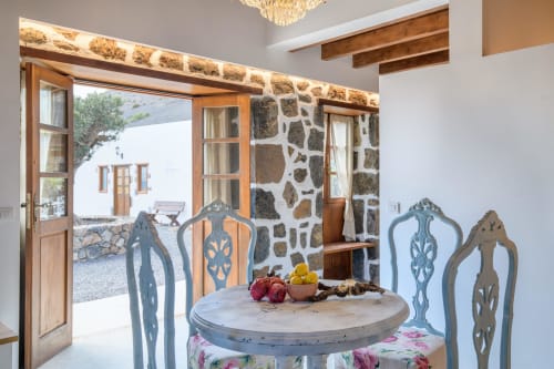 Dining area in El Granero cottage at Finca de La Geria, Yaiza, with blue ornate chairs and stone walls opening to garden