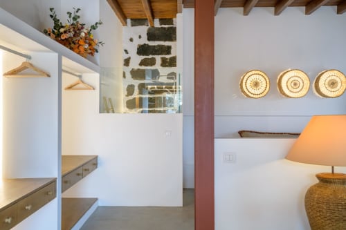 El Granero cottage bedroom at Finca de La Geria with white walls, orange lamp, woven wall décor, and garden views in Yaiza