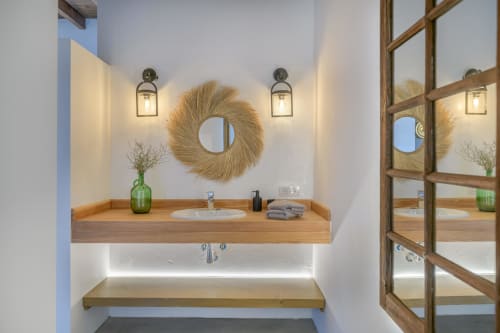 Modern bathroom vanity with wooden counter, woven mirror, and dual sconces at Finca de La Geria cottage