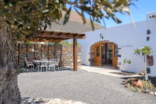 La Cochera cottage at Finca de La Geria in Yaiza, Spain features a white-walled structure with wooden door, garden seating