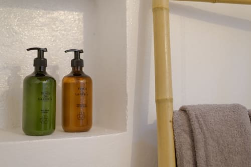Bathroom amenities at Finca de La Geria cottage: green and amber pump bottles beside folded towel and bamboo fixture