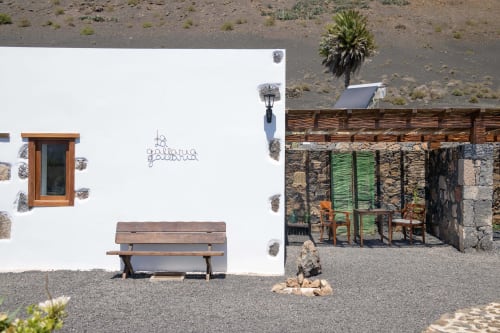 Rustic cottage courtyard at Finca de La Geria with wooden bench, white walls, and desert garden view in Yaiza