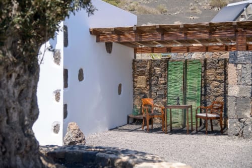 Cottage patio at Finca de La Geria with wooden pergola, green shutters, stone walls, and orange chairs in Yaiza