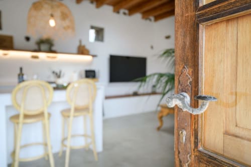 Open wooden door to La Gallania cottage at Finca de La Geria, revealing bright living room with kitchen, cream chairs, and