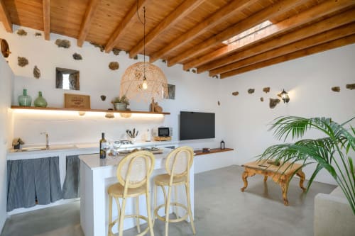 Modern cottage kitchen-dining area at Finca de La Geria with wooden beams, white counters, rattan pendant light, and garden