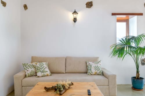 Bright living room at Finca de La Geria cottage with beige sofa, decorative pillows, wooden table, potted palm plant, and