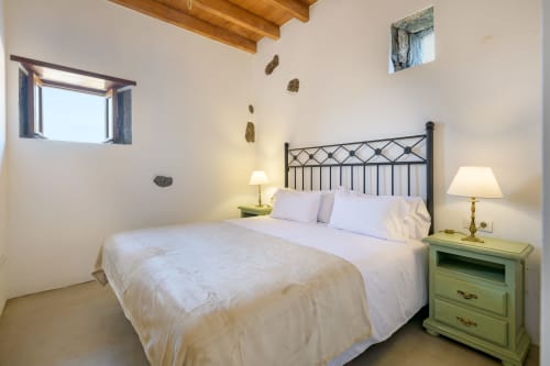 Spacious bedroom at Finca de La Geria cottage in Yaiza with queen bed, wrought iron headboard, green nightstands, wooden