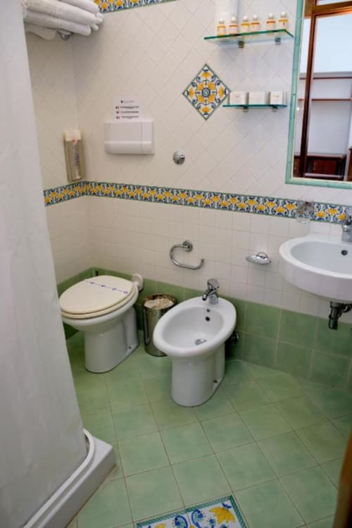 Bagno dell'Hotel Principe di Rinella con pavimento in piastrelle verdi, bidet, toilette, lavabo su colonna e decorazioni giallo-blu
