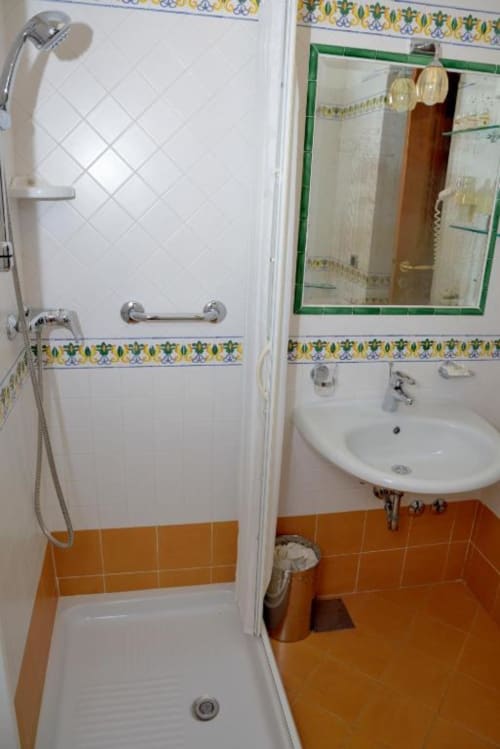 Bagno dell'Hotel Principe di Rinella con piastrelle bianche, pavimento arancione, doccia, lavabo, specchio e bordo decorativo