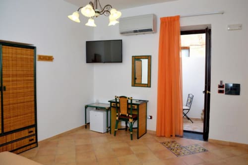 Camera tripla dell'Hotel Principe di Rinella con scrivania, sedia, TV a schermo piatto, aria condizionata e tende arancioni a Rinella,