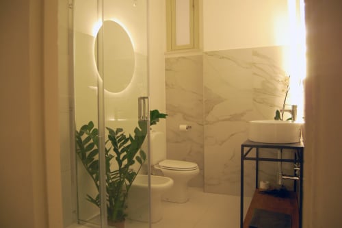 Moderno bagno della struttura ricettiva a Catania con pareti in marmo, specchio rotondo illuminato, box doccia in vetro e pianta in vaso