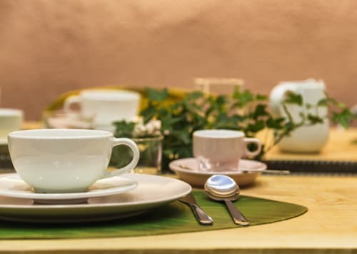 Tavolo elegantemente apparecchiato con stoviglie in ceramica bianca, sottopiatto verde e posate presso Todo Sicily B&B a Catania