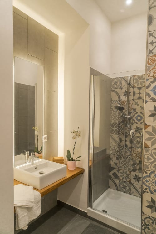 Bagno moderno in B&B siciliano con lavabo bianco su mobile in legno, specchio illuminato e doccia con piastrelle decorate