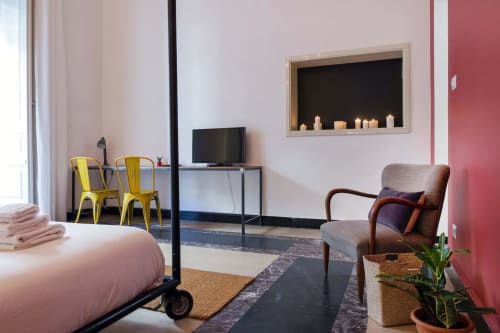 Camera moderna B&B a Catania con parete accent rosa, letto, sedie gialle, scrivania TV e poltrona con nicchia con candela