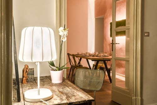 Scrivania moderna con lampada a sospensione bianca, pianta di orchidea e sedia in legno nella camera B&B di Catania con pareti color corallo