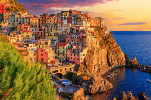 Villaggio colorato sulla scogliera al tramonto con vista sul Mar Mediterraneo e barche nel porto