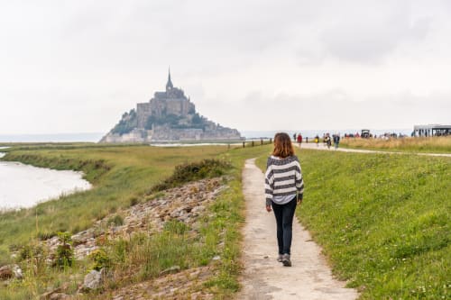 Femme jogging vers le Mont-Saint-Michel avec les marais verts et les eaux de marée en Normandie