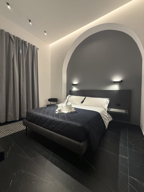 Camera Deluxe Moderna presso l'hotel boutique Volta 70 a Napoli con parete ad arco, letto nero, biancheria bianca e luce ambientale