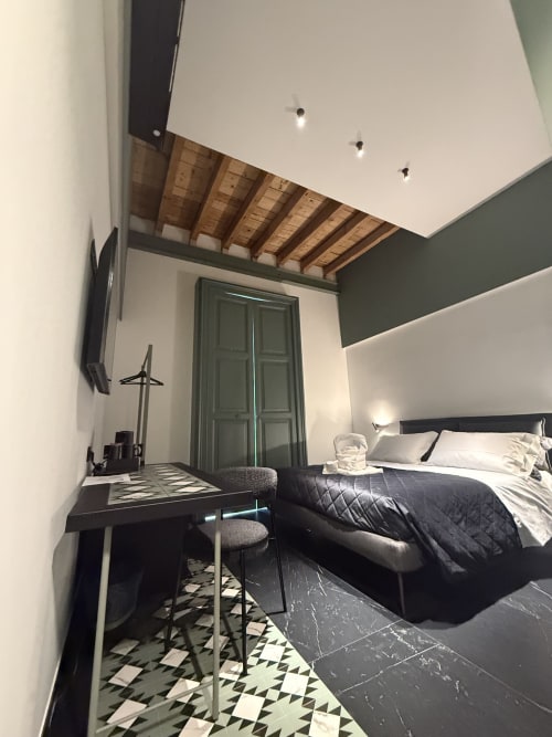 Camera deluxe moderna di Volta 70 Napoli con letto queen size, scrivania, TV, piastrelle geometriche e parete verde salvia