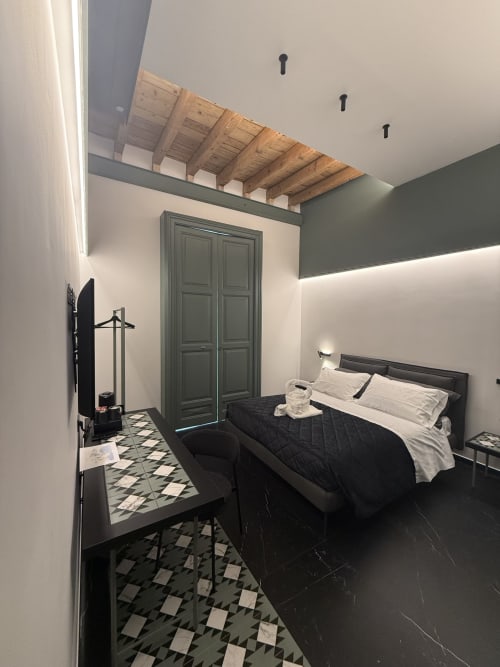 Camera da letto lusso moderna a Volta 70 Napoli con letto nero, armadio verde, travi in legno a vista e mattonelle geometriche