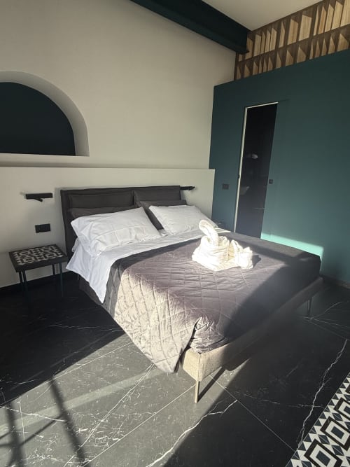 Camera moderna con letto matrimoniale, design minimalista, pavimento in marmo scuro e parete turchese a Napoli