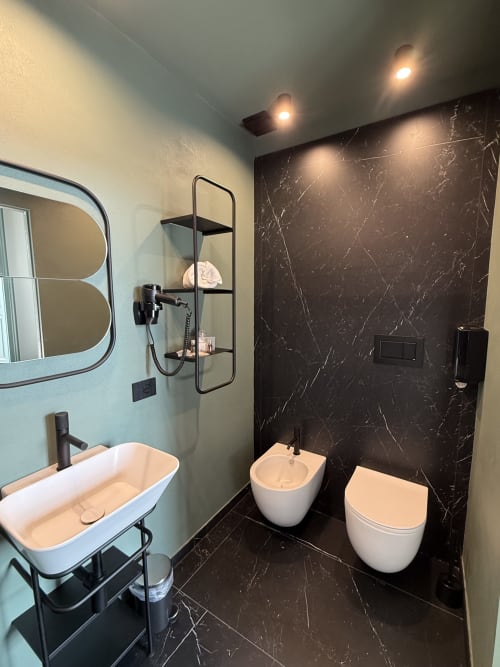 Bagno moderno in Volta 70 Napoli con pareti in marmo, sanitari bianchi, bidet, WC, lavabo con rubinetto nero e doccia