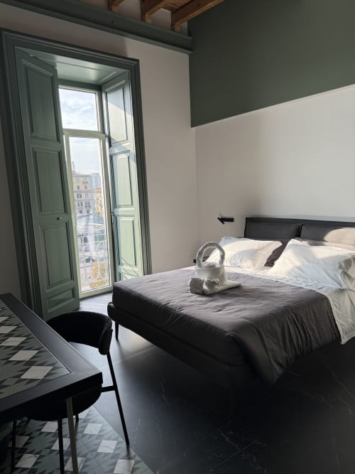 Lussuosa camera doppia a Volta 70 Napoli con balcone vista città, letto moderno scuro e porte con persiane verdi