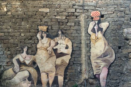 Colorful street art mural on stone wall in Orosei featuring stylized figures in earthy tones