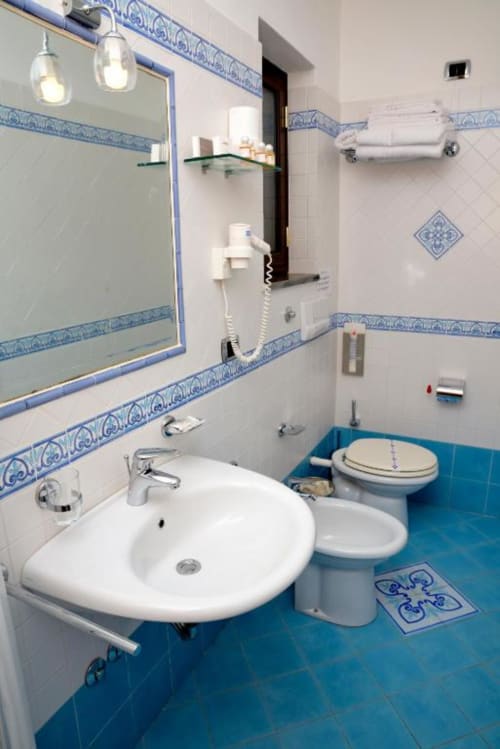Bagno moderno con lavabo bianco, water, bidet, pavimento in piastrelle blu e decorativi rivestimenti blu e bianchi all'Hotel Principe di