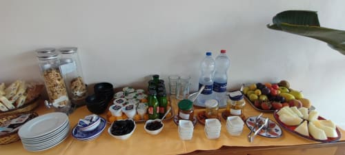 Buffet colazione all'Hotel Principe di Rinella con frutta fresca, formaggi, cereali, pane, olive, bevande e stoviglie