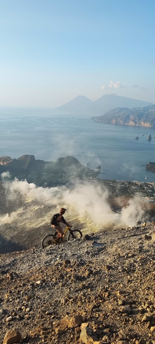 Ciclista su terreno vulcanico con vista su Rinella, isole lontane e mare