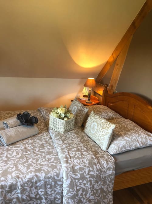 Chambre de charme très cosy du gite Vert Campagne avec literie à motifs lin, coussins décoratifs, serviettes de bain roulées et ambiance chaleureuse