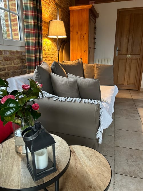 Séjour chaleureux du gite avec canapé taupe, table en bois et éclairage ambiant