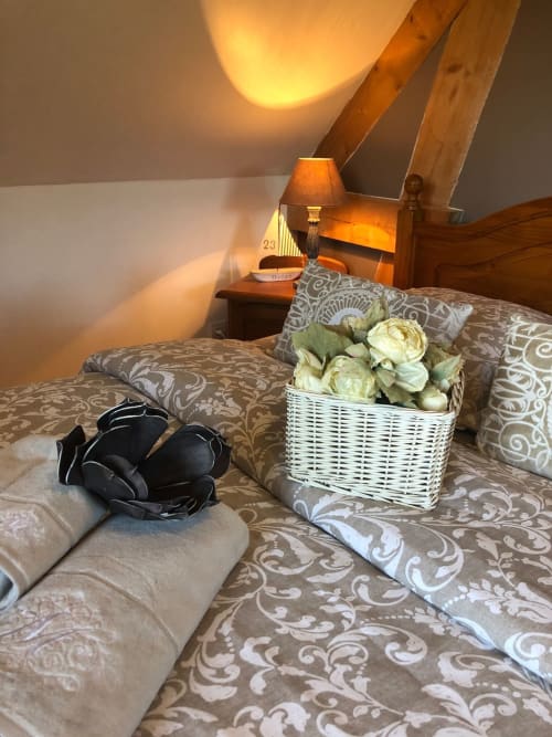 Chambre accueillante du gite Le Clos Mahiel avec parure à motifs lin, panier fleuri en rotin blanc, poutres apparentes, ambiance chaleureuse 